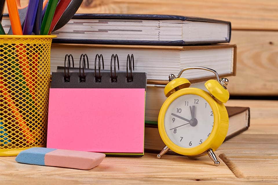 Back to school concept with school supplies. Office desk with alarm clock, blank notebook, pile of books and colorful pencils. Concept of education.