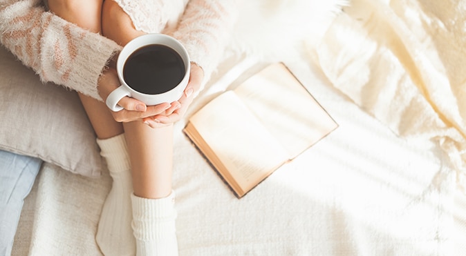 Aerial shot of woman holding coffee in bed with book, Better Sleep Council