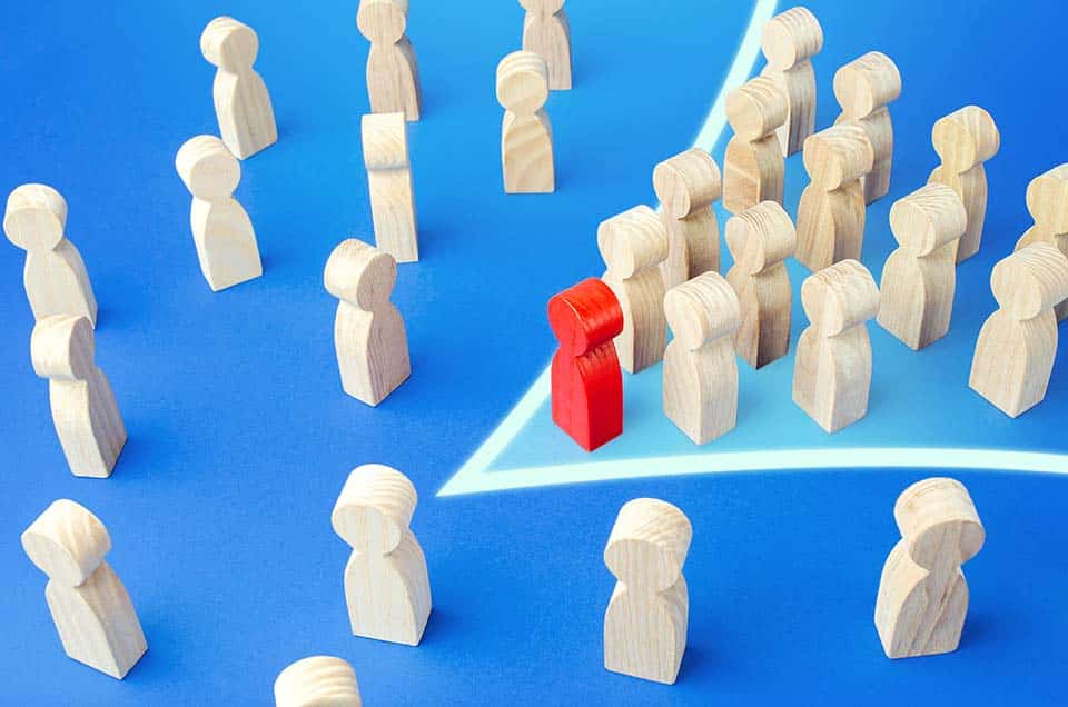 Small wooden models representing people with one red one that is leading a group of them