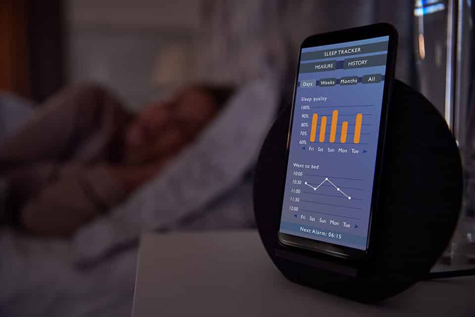 Sleep and Technology: How It Affects Sleep Quality 1 Woman Sleeping In Bed With Sleep Data App Running On Mobile Phone On Bedside