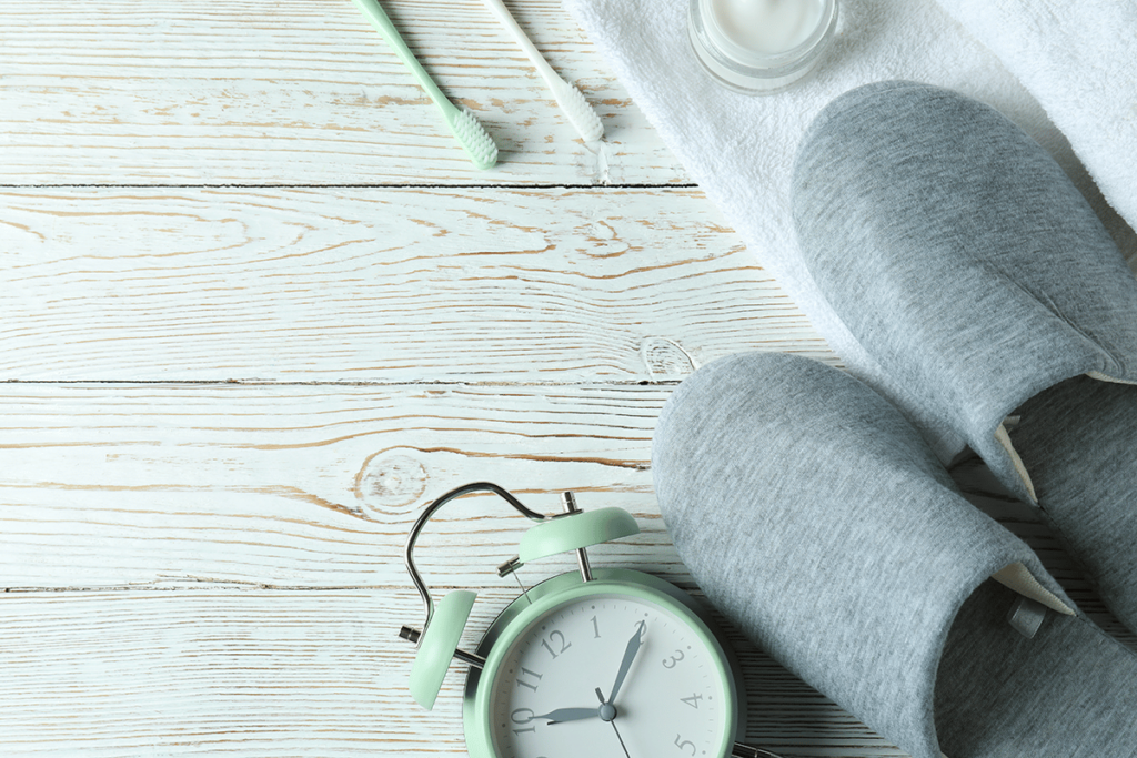 a pair of soft slippers rest on top of a towel with a toothbrush and alarm clock